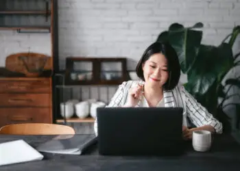 Young Asian woman having online business meeting, video conferencing on laptop with her business partners, working from home in the living room