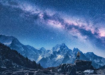 Silhouette of a standing man on the stone, mountains and starry sky with Milky Way at night in Nepal. Sky with stars. Travel. Night landscape with snow-covered mountain ridge and milky way. Space